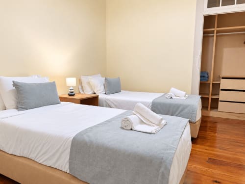 Twin bedroom at Check Madeira hotel in Ribeira Brava with white and gray bedding, wooden floors, and closet storage.