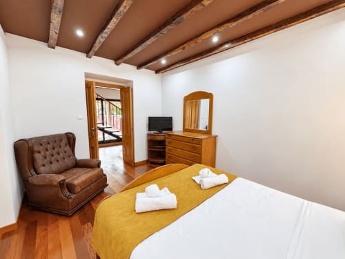 Spacious bedroom at Check Madeira hotel in Ribeira Brava with wooden beams, brown leather chair, and modern amenities