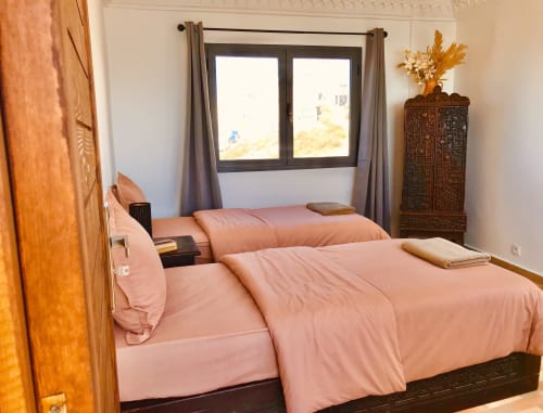 Bright bedroom with twin beds, pink linens, sea view windows, wooden accents at Imsouane Surf Paradise hotel