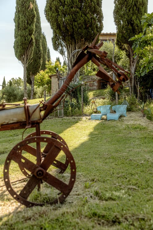 Antichi macchinari agricoli nel giardino di villa toscana con cipressi e sedie blu, Buonconvento
