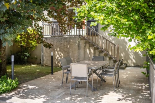 Shaded patio dining area at Domaine Des Escouanes cottage with table, chairs, and lush garden views