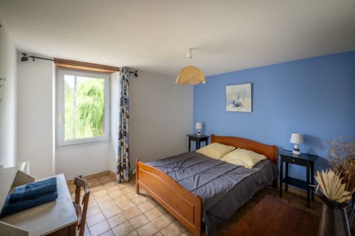 Bright bedroom at Domaine Des Escouanes cottage with blue walls, wooden bed, garden view window, and modern amenities