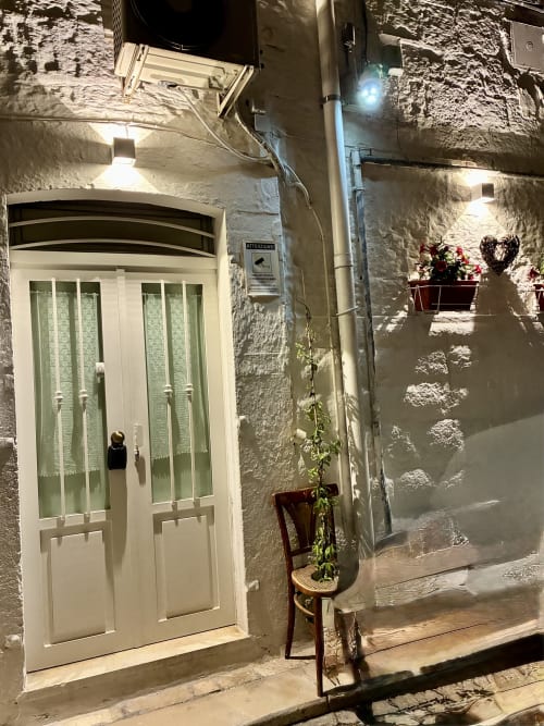 Affascinante ingresso con porta bianca dell'appartamento La piccola casa di Tania a Terlizzi, Italia, vicoletto illuminato la sera con vasi di fiori