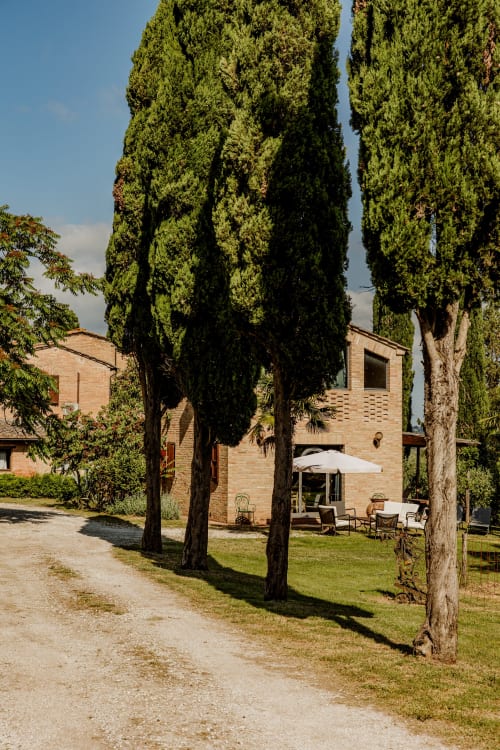 Hotel toscano a Buonconvento con alti cipressi, edificio in laterizio e area patio con posti a sedere