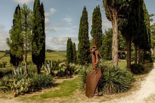 Viale di cipressi toscani con scultura metallica rustica nei giardini dell'hotel di Buonconvento, Italia