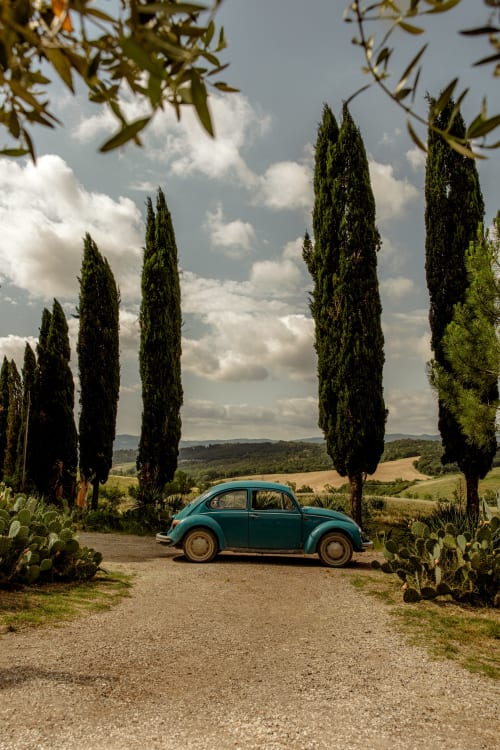 Maggiolone turchese parcheggiato su strada toscana alberata vicino a Buonconvento con colline ondulate