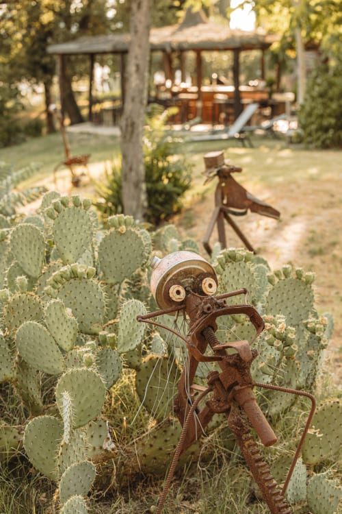 Scultura in metallo rustico tra i fichi d'india nel giardino toscano dell'hotel Quarantallina