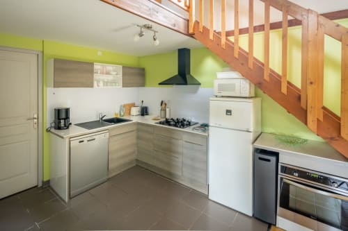 Cuisine moderne du Domaine Des Escouanes avec murs vert citron, escalier en bois et électroménagers inox