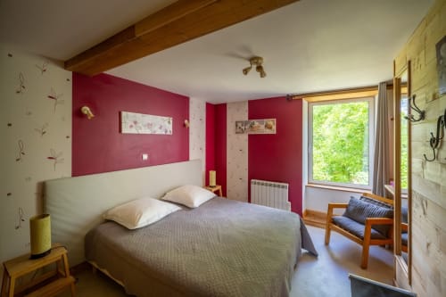 Chambre lumineuse au Domaine Des Escouanes avec murs bordeaux, lit queen-size, poutres apparentes et vue sur le jardin