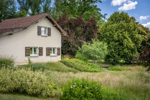 Maison de charme couleur crème au Domaine Des Escouanes à Prudhomat, entourée de jardins luxuriants et d'arbres