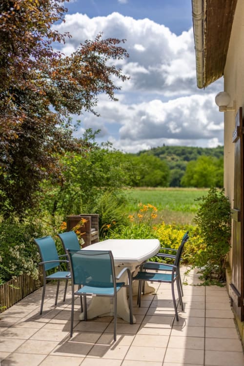 Terrasse avec table à manger et chaises bleues surplombant les champs verdoyants du gîte Domaine Des Escouanes, Prudhomat
