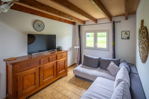 Salon cosy du Domaine Des Escouanes avec canapé, meuble TV en bois et vue sur le jardin par les portes-fenêtres