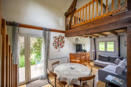 Séjour ouvert du gîte Domaine Des Escouanes avec table à manger, canapé, poutres apparentes et vue sur le jardin