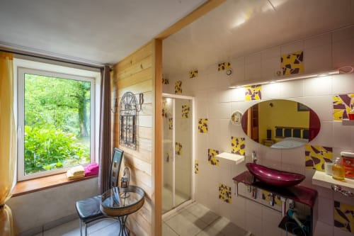 Salle de bains colorée au gîte Domaine Des Escouanes avec carrelage jaune et bordeaux, fenêtre vue jardin, lavabo et vanité modernes