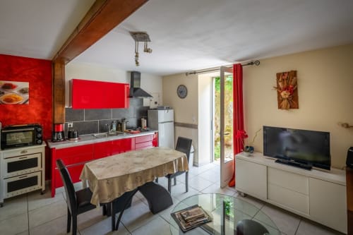 Cuisine-séjour contemporain ouvert du Domaine Des Escouanes avec armoires rouges, table à manger, TV et vue sur le jardin