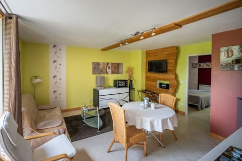 Salon lumineux jaune vif au Domaine Des Escouanes avec table à manger, chaises en rotin et meuble de divertissement en bois