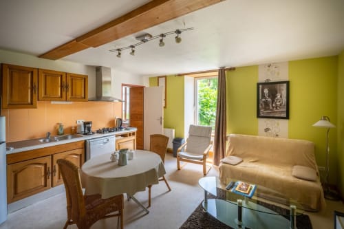 Séjour ouvert et lumineux avec murs vert citron, cuisine en bois, table ronde et canapé beige au Domaine Des