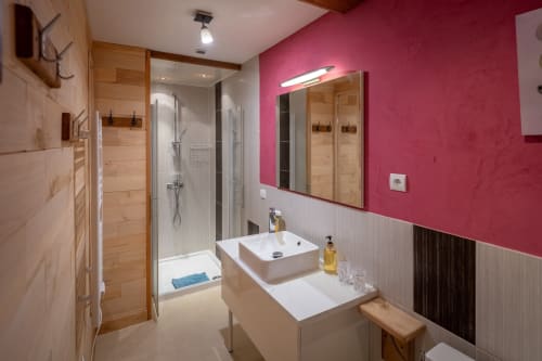 Salle de bain moderne aux murs roses, vanité en bois, vasque à poser, miroir éclairé et douche à l'italienne Domaine Des