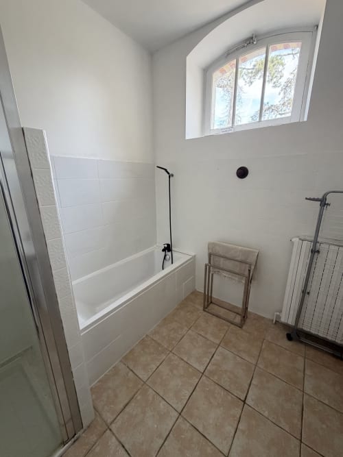 Modern bathroom at Les gites de Lereau with white tile bathtub, heated towel rack, and arched window overlooking the garden.