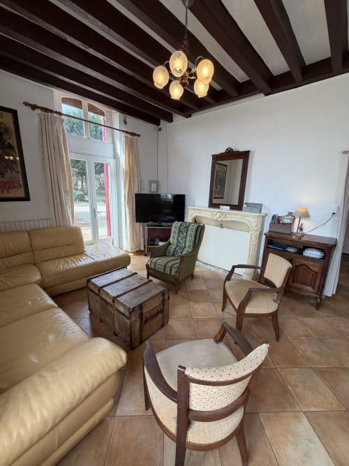 Spacious living room at Les gites de Lereau with beamed ceiling, leather sofa, fireplace, and garden views