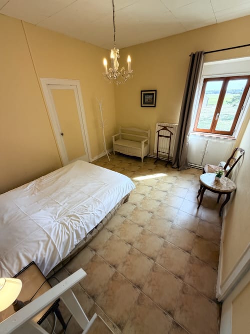 Bright yellow bedroom at Les gites de Lereau with tiled floor, white bed, crystal chandelier, and rustic furnishings