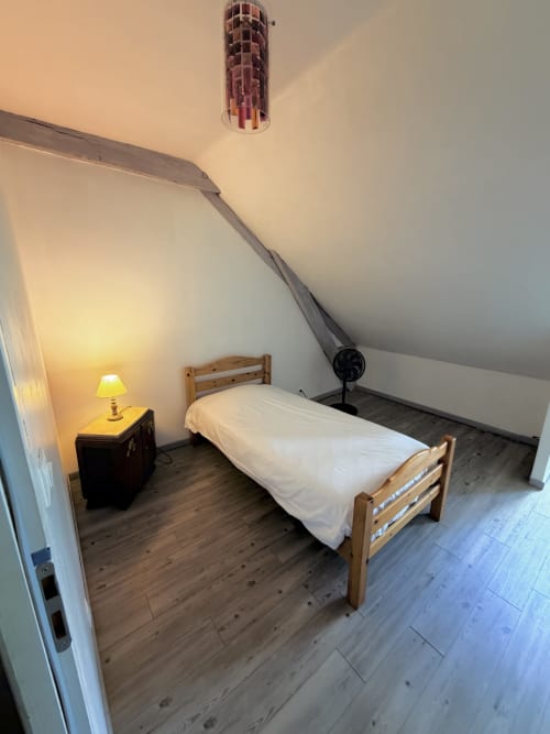 Cozy attic bedroom at Les gites de Lereau with wooden bed, lamp, and sloped ceiling in Vallières-les-Grandes