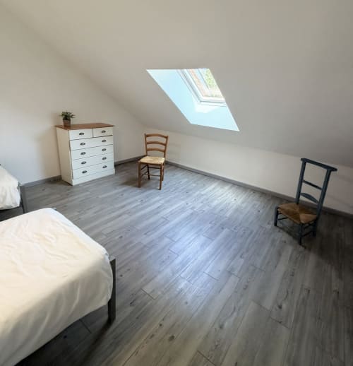Bright attic bedroom at Les gites de Lereau with skylight, wooden floors, white dresser, and rustic chairs