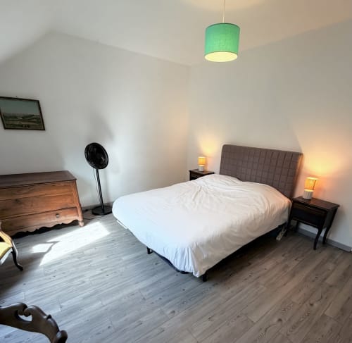 Bright bedroom at Les gites de Lereau with white bedding, gray upholstered headboard, wooden furniture, and green pendant