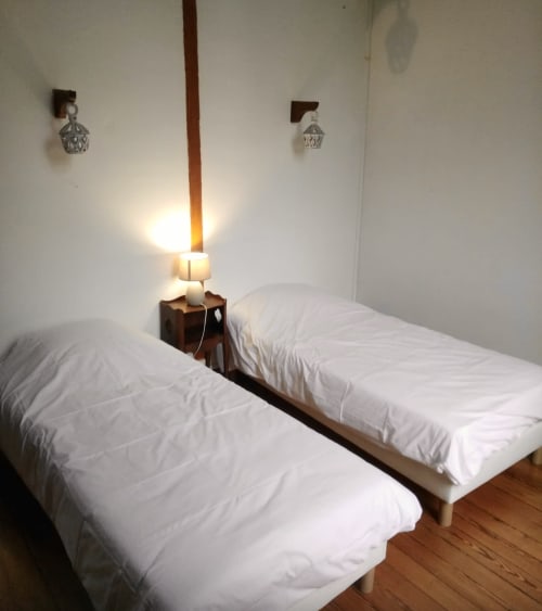 Chambre double aux Gîtes de Lereau avec draps blancs, table de nuit en bois et appliques murales à Vallières-les-Grandes
