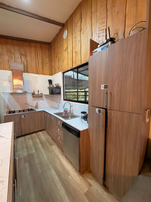 Cocina moderna en villa Volcán Irazú de Chalets Vistas del Poás con gabinetes de madera, cubierta blanca y acero inoxidable
