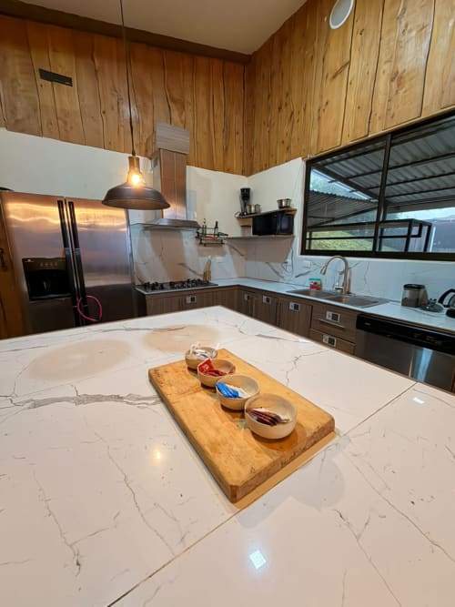 Cocina moderna con encimeras de mármol, isla de madera con cuencos, electrodomésticos de acero inoxidable y techo de madera en Volcán