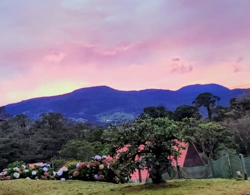 Vista al atardecer desde villa Volcán Irazú en Chalets Vistas del Poás, Heredia, con montañas y jardín florecido