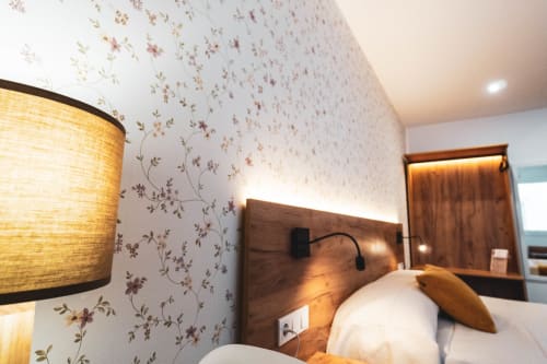 Acogedora habitación del Hostal Restaurante Angel en Huelma con papel tapiz floral, cabecero de madera e iluminación cálida