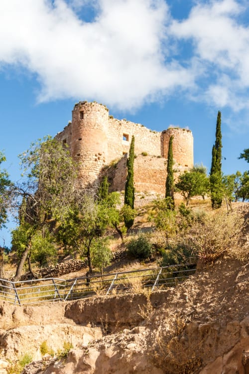 Ruinas de fortaleza medieval de piedra en Huelma, Jaén, rodeadas de cipreses y paisaje árido cerca del Hostal Restaurante Angel