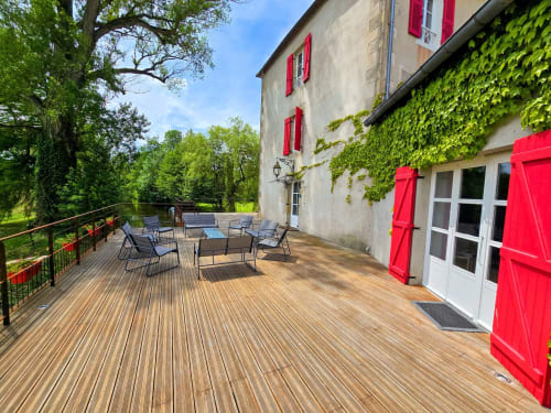 Spacious wooden deck terrace at Le Moulin des Ducs cottage in Epinac with red shutters, river views, and lounge seating