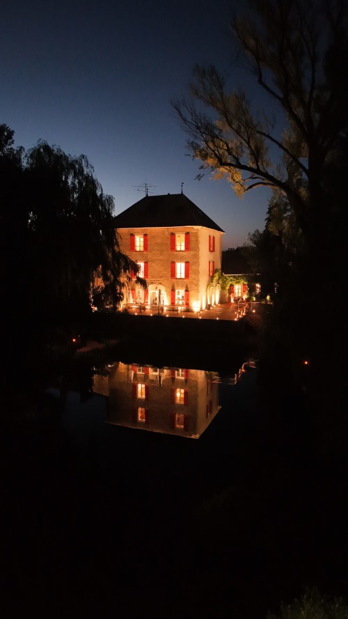 Le Moulin des Ducs cottage at dusk, illuminated in warm orange light with river reflection, Epinac B&B