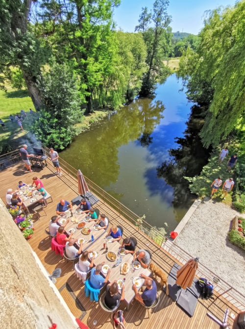Des clients dînant sur la terrasse riveraine de Vindihouses Epinac, arbres luxuriants et reflets bleus de l'eau