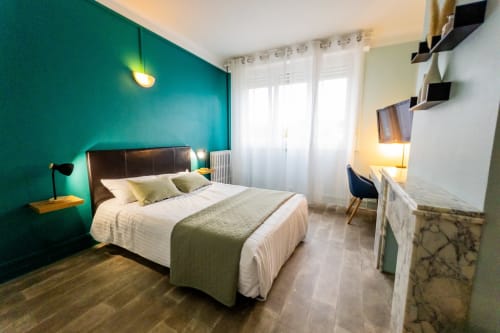 Chambre moderne de l'Hôtel Joly à Armentières avec mur d'accent turquoise, lit queen, bureau et vue sur le jardin