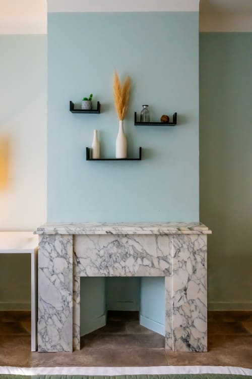 Mur bleu clair avec étagères flottantes noires présentant des vases blancs et des herbes de la Pampa séchées au-dessus d'une cheminée en marbre à l'hôtel