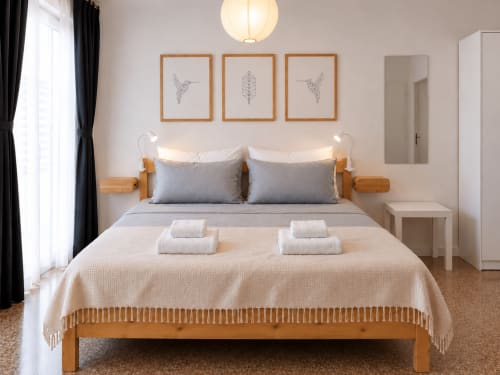 Camera moderna presso Easystay Bari con letto in legno, cuscini grigi, biancheria bianca e arte murale minimalista