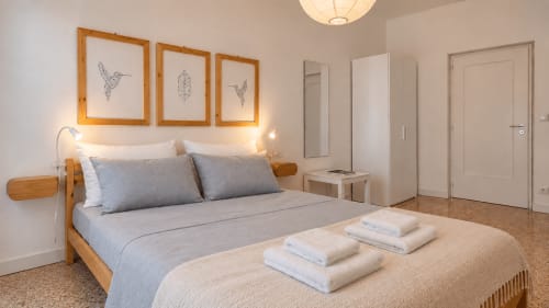 Camera moderna presso Easystay Bari con letto in legno, biancheria blu, opera d'arte colibrì e illuminazione calda