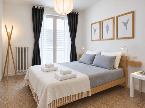 Camera moderna presso Easystay Bari Apartment con letto in legno, tende nere e quadro con uccelli incorniciato su pareti bianche