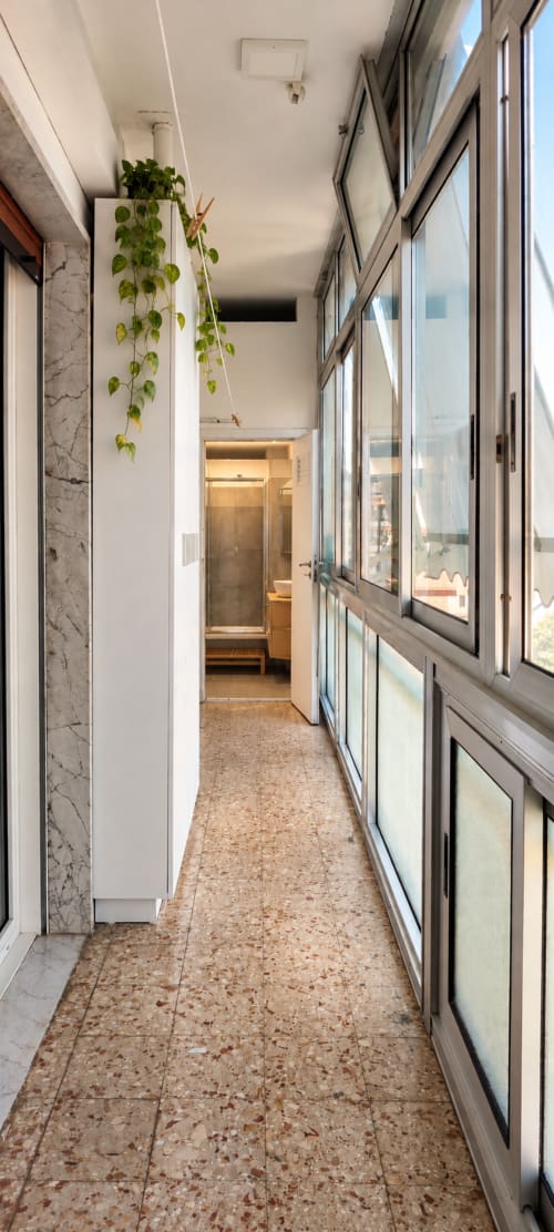 Corridoio luminoso dell'appartamento Easystay Bari con pavimento in sughero, ampie finestre, parete in marmo e pianta verde sospesa