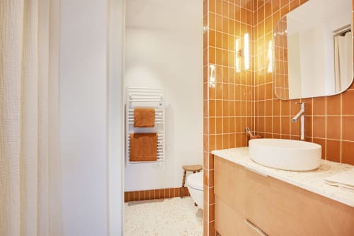 Salle de bain moderne dans un appartement de Montmartre avec carrelage orange, vasque blanche, meuble en bois et porte-serviettes chauffant