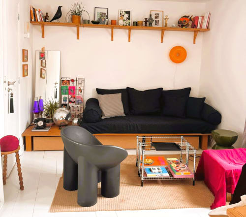 Salon d'un appartement montmartrois avec canapé noir, touches d'orange et étagères en bois à Paris