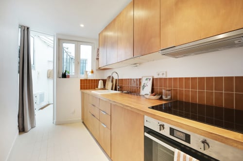 Cuisine moderne avec armoires en bois, cuisinière noire et dosseret en carrelage terracotta dans un appartement montmartrois à Paris