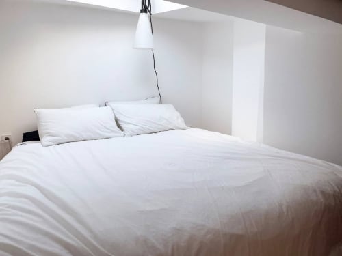 Chambre minimaliste blanche dans un appartement montmartrois avec luminaire suspendu moderne et linge de lit épuré