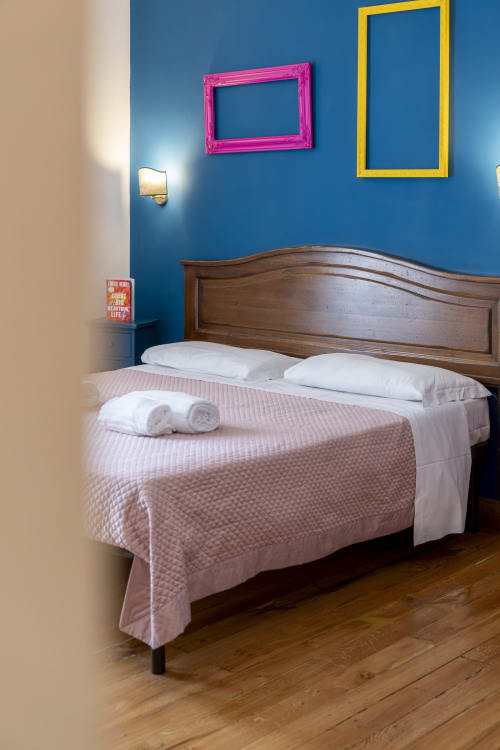 Camera luminosa a Pepe's Place Roma con muri blu, cornici colorate, letto in legno e biancheria rosa