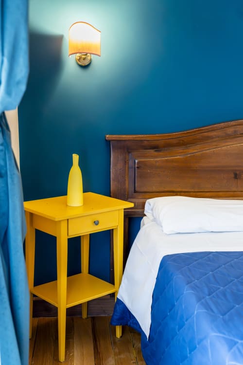 Camera luminosa a Pepe's Place Roma con pareti blu, comodino giallo, letto in legno e applique da parete
