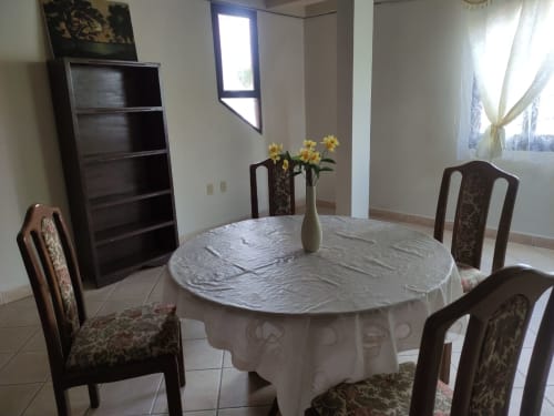 Elegante comedor en Wehost Costaluz de Tarija con mesa redonda, sillas tapizadas, flores y ventanas luminosas